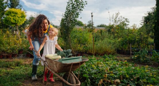 A mother and daughter pushing a wheelbarrow together.