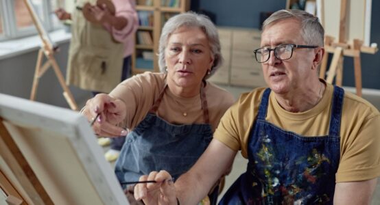 An older couple painting at an easel together.