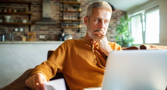 A man in his 50s thinking while using a laptop